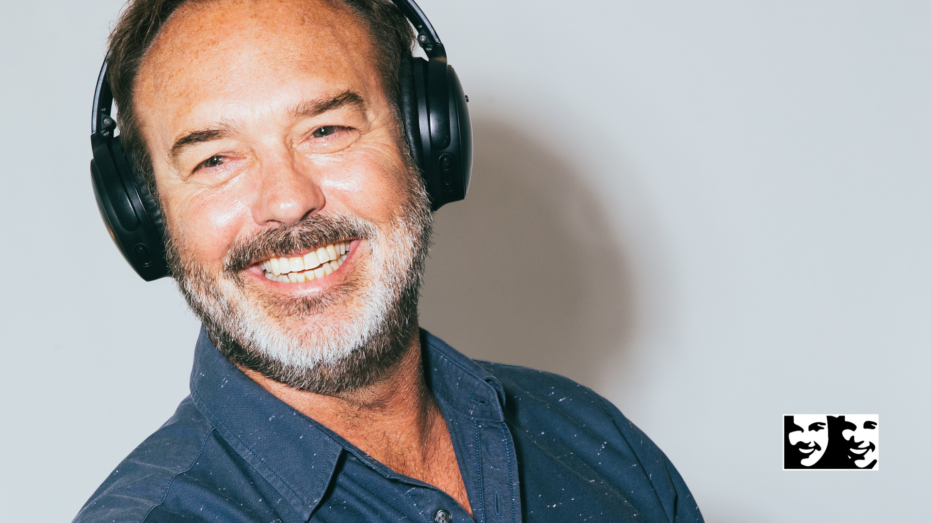Man wearing headphones, smiling broadly against a white background, wearing a blue shirt.