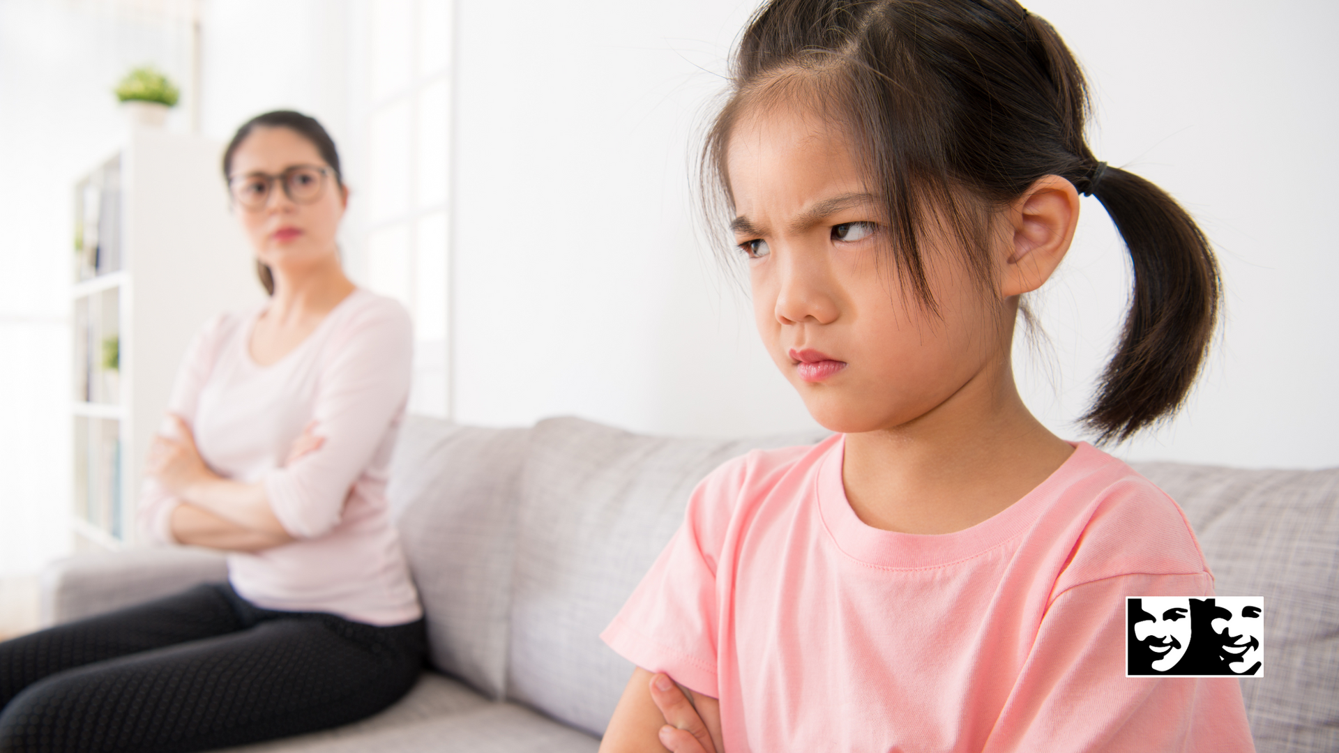 A little girl is sitting on a couch with her arms crossed and looking at the camera.