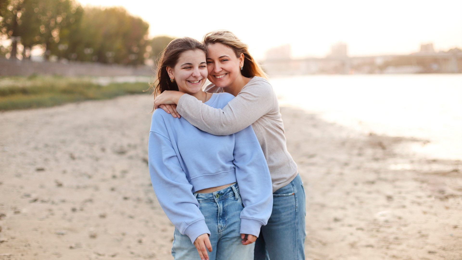 A mother and daughter are hugging each other on the beach.