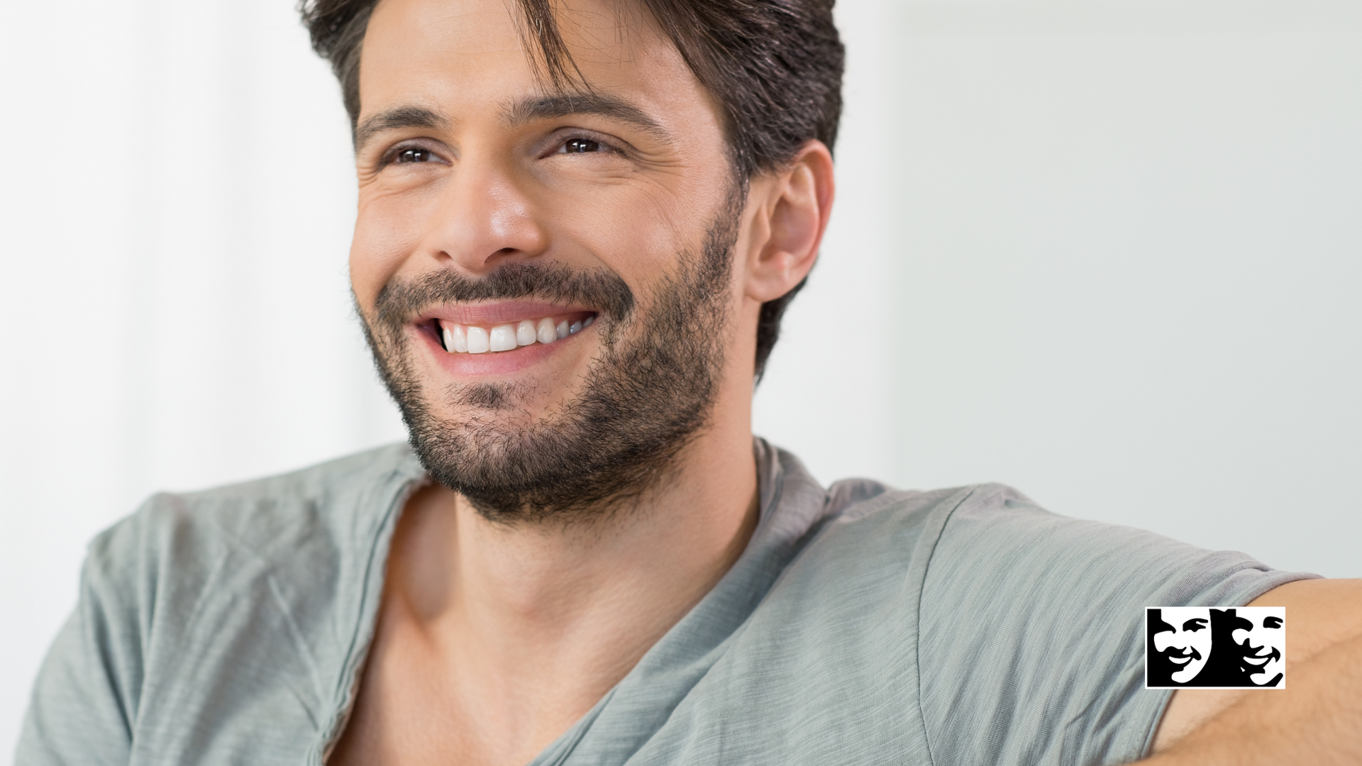 A man with a beard is smiling and wearing a grey shirt.