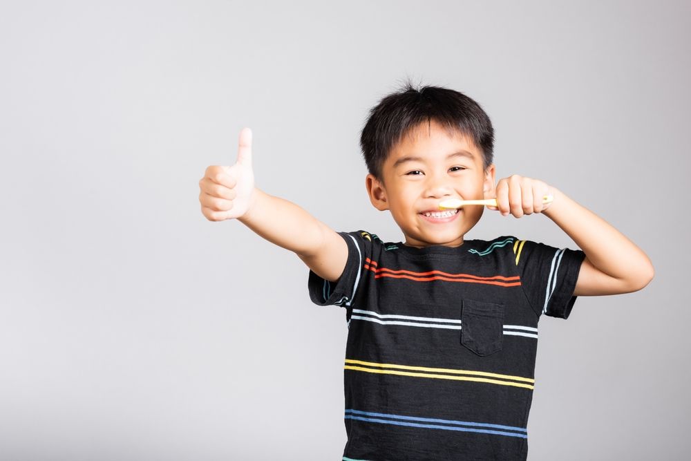 A young boy is brushing his teeth and giving a thumbs up.
