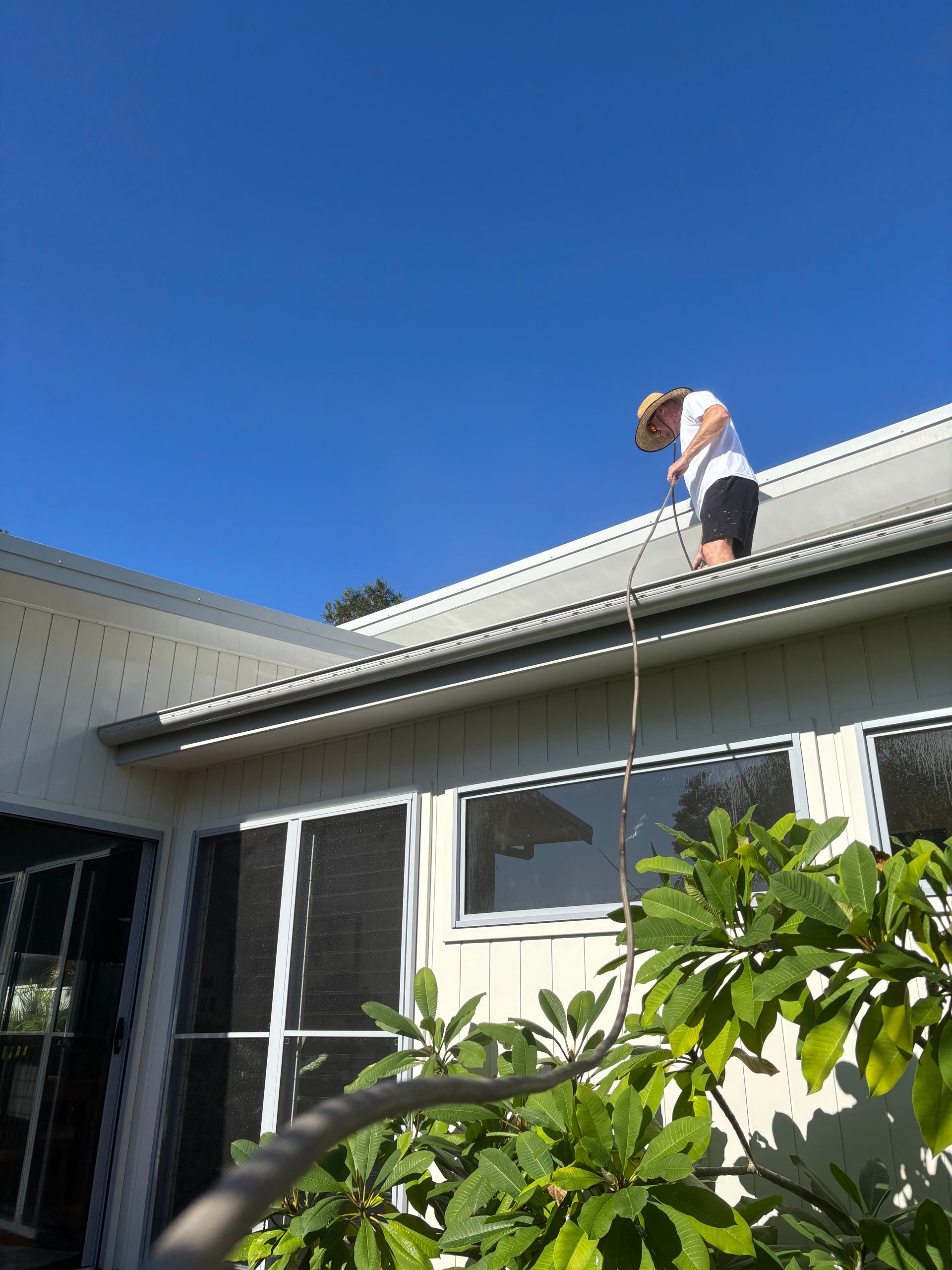 A Man is Painting the Gutters of a House With a Brush — Timeless Painting In Gosford, NSW