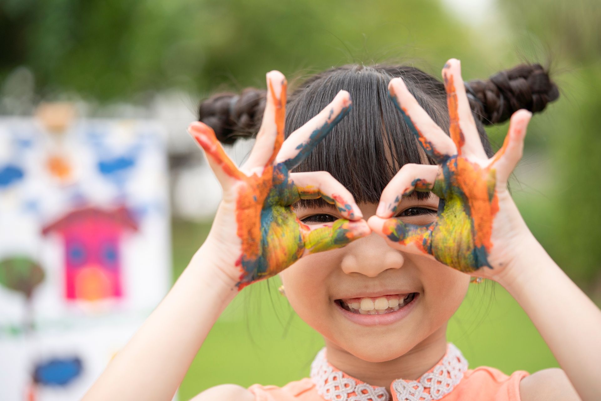 A smiling child with painted hands poses playfully during a colorful outdoor art activity. A smiling child with painted hands poses playfully during a colorful outdoor art activity.