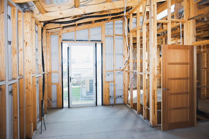 The interior of a house under construction with visible wooden framing, unpainted walls, and a new wooden door.