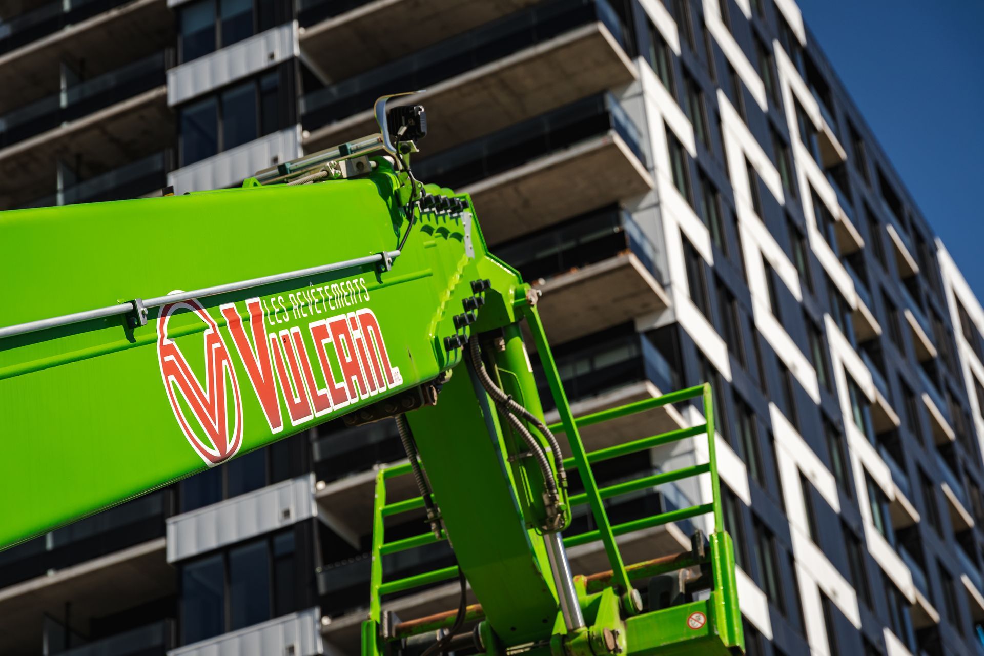 Télésiège vert avec logo "Vertima", devant un immeuble moderne de grande hauteur.