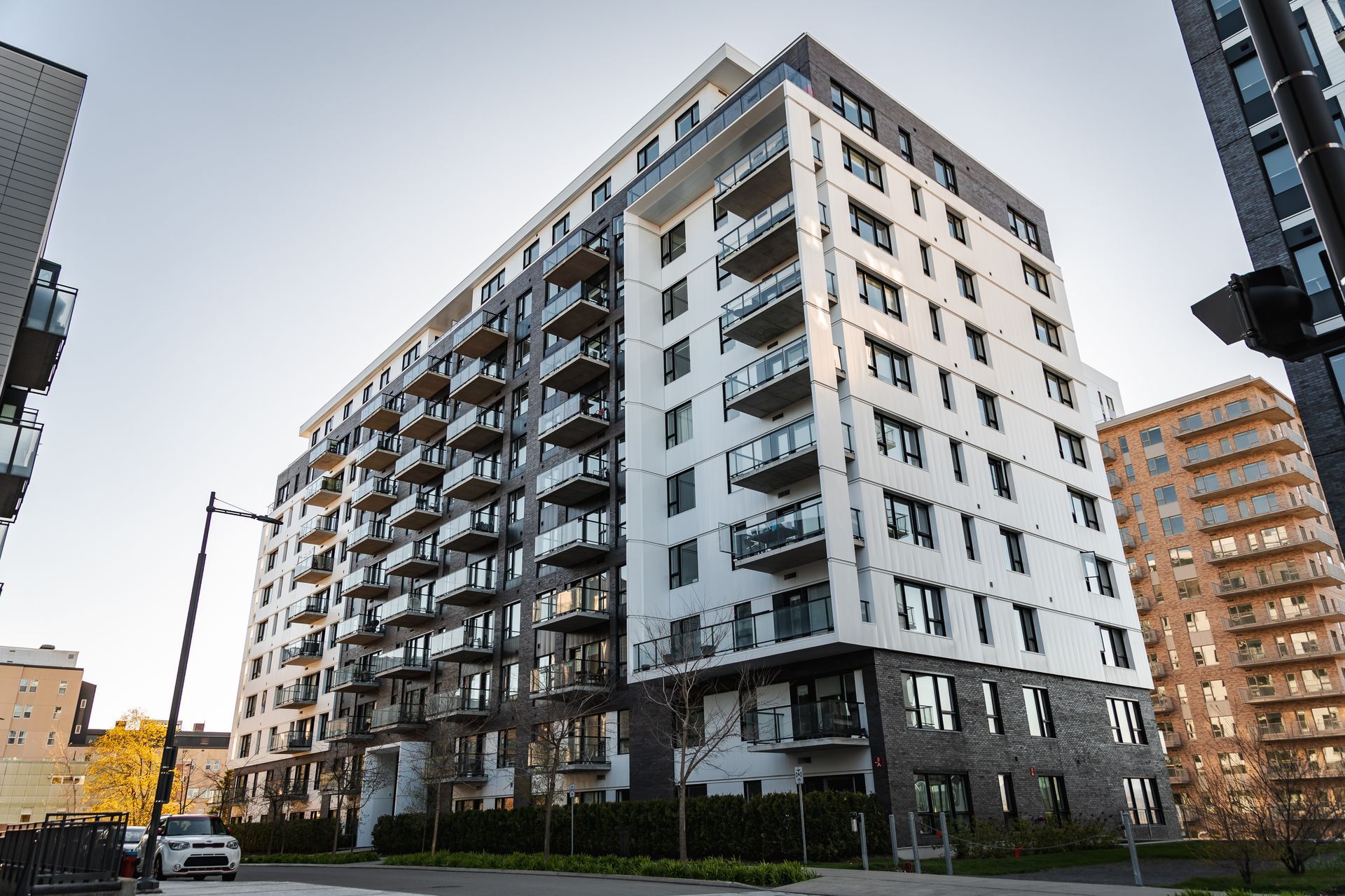 Immeuble d'appartements moderne avec balcons, façade blanche et grise, journée ensoleillée.