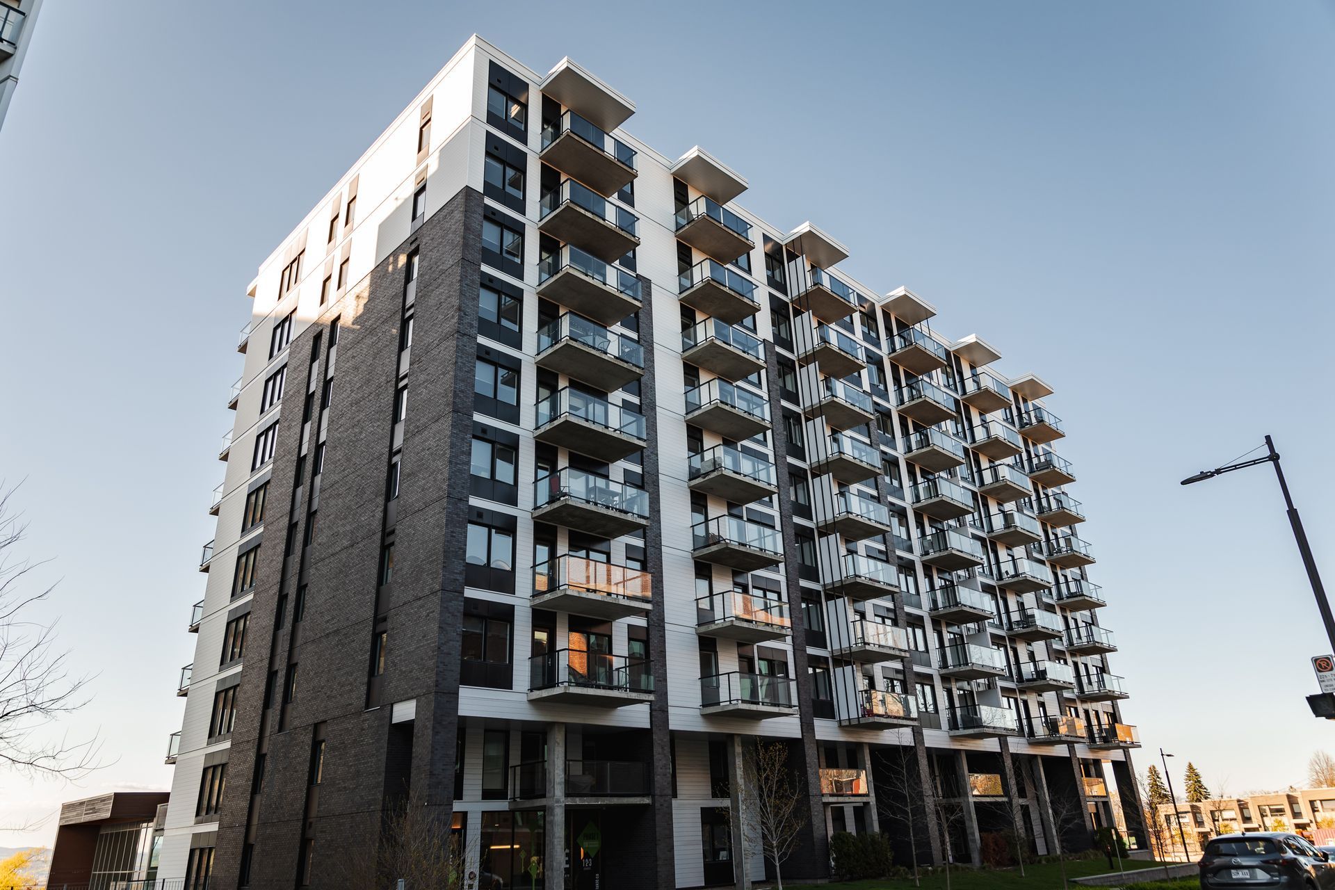 Immeuble d'appartements moderne, gris et blanc avec plusieurs balcons, sous un ciel bleu.