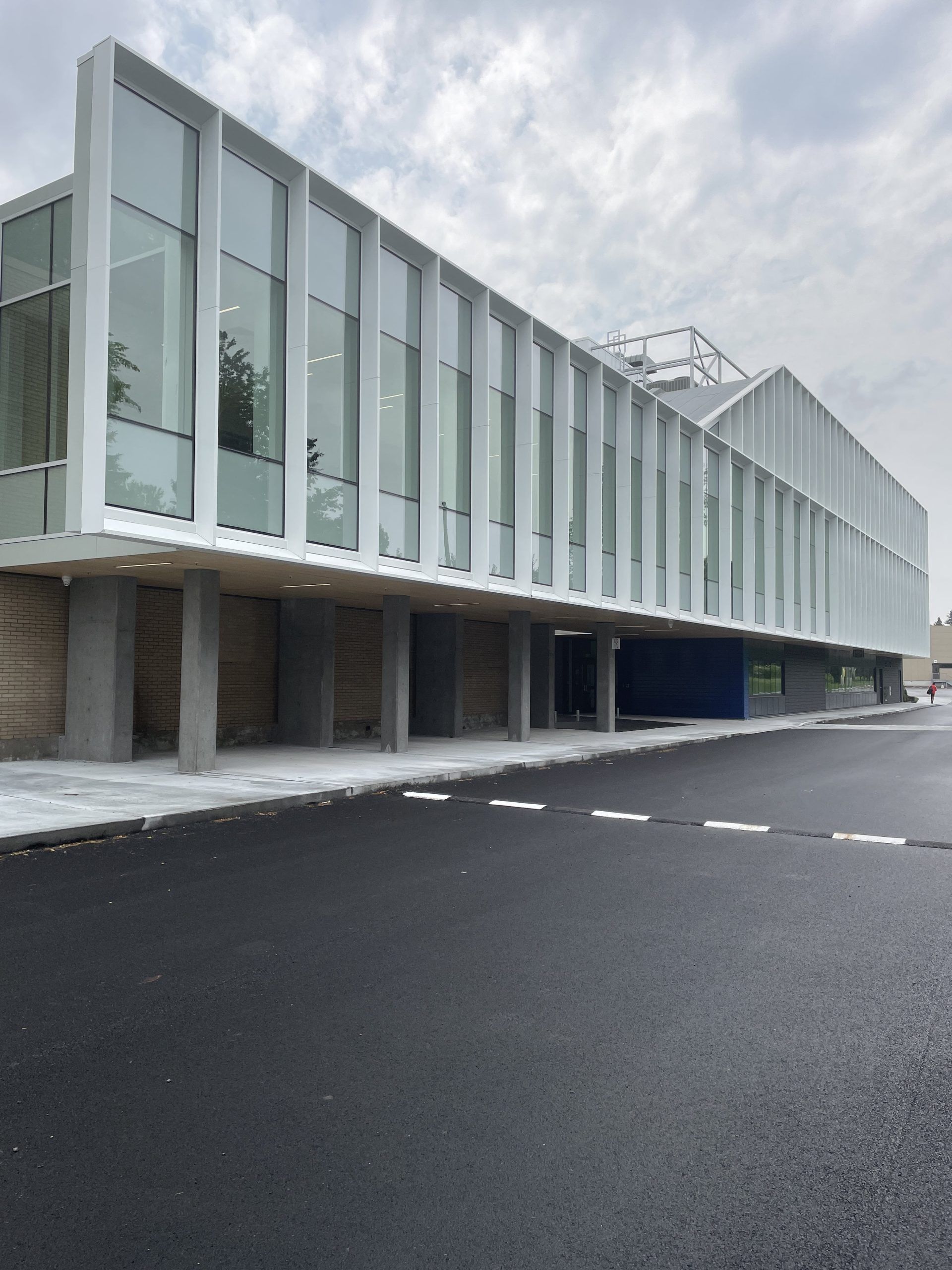 Bâtiment moderne de deux étages avec panneaux verticaux blancs et grandes fenêtres ; ciel couvert.