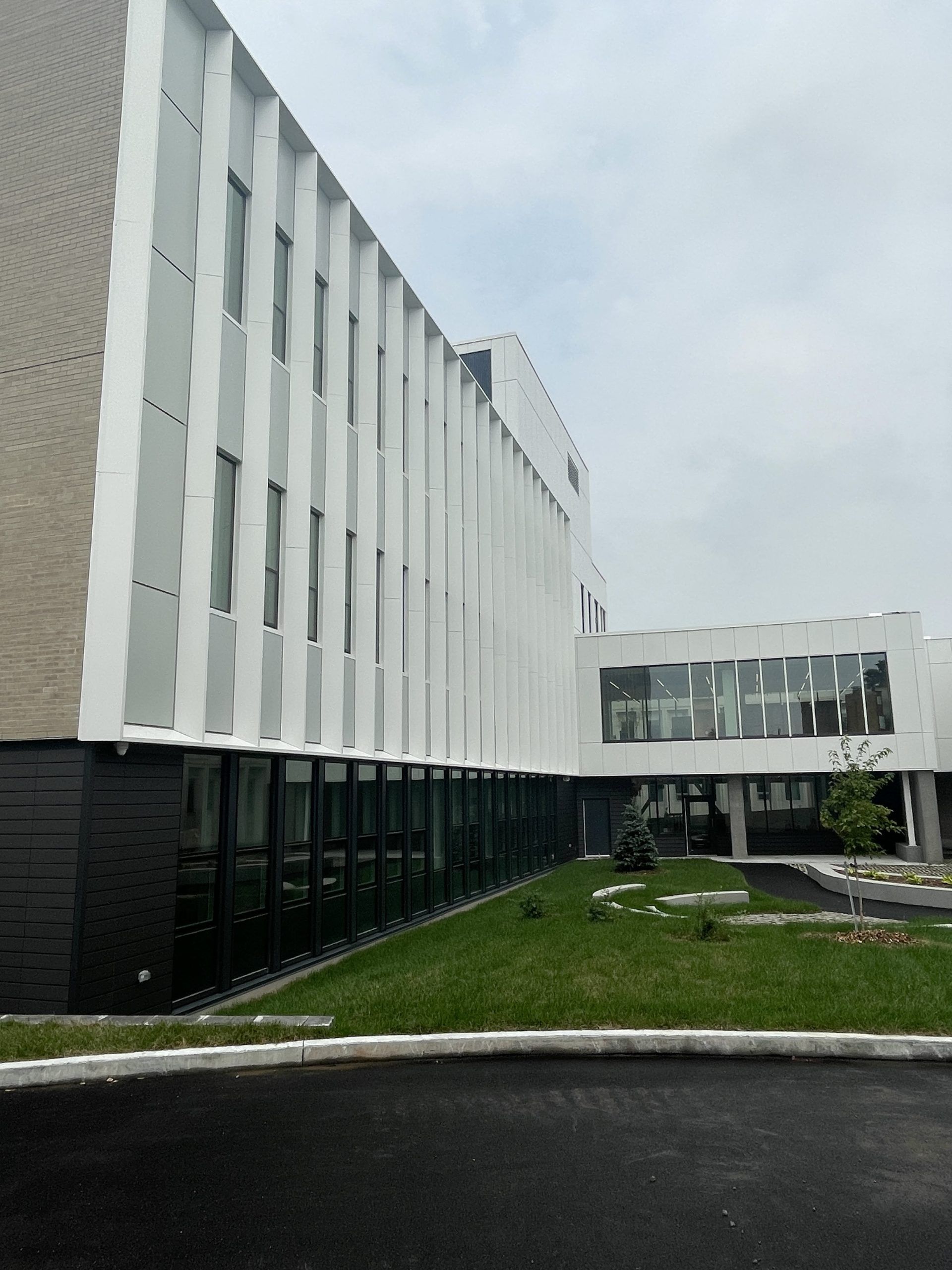 Bâtiment moderne à la façade blanche, avec de longues fenêtres et un pont de liaison. Devant, une pelouse verte.