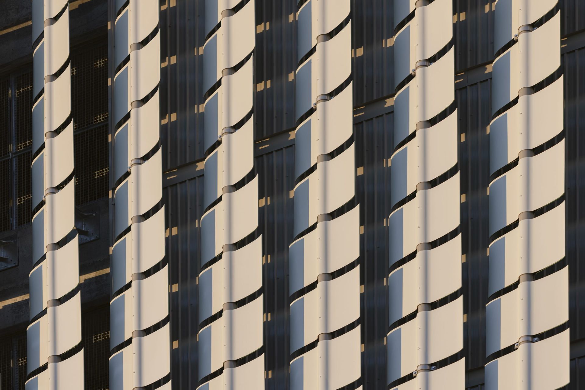 Façade de bâtiment blanche et noire avec des panneaux courbes alternés projetant des ombres.