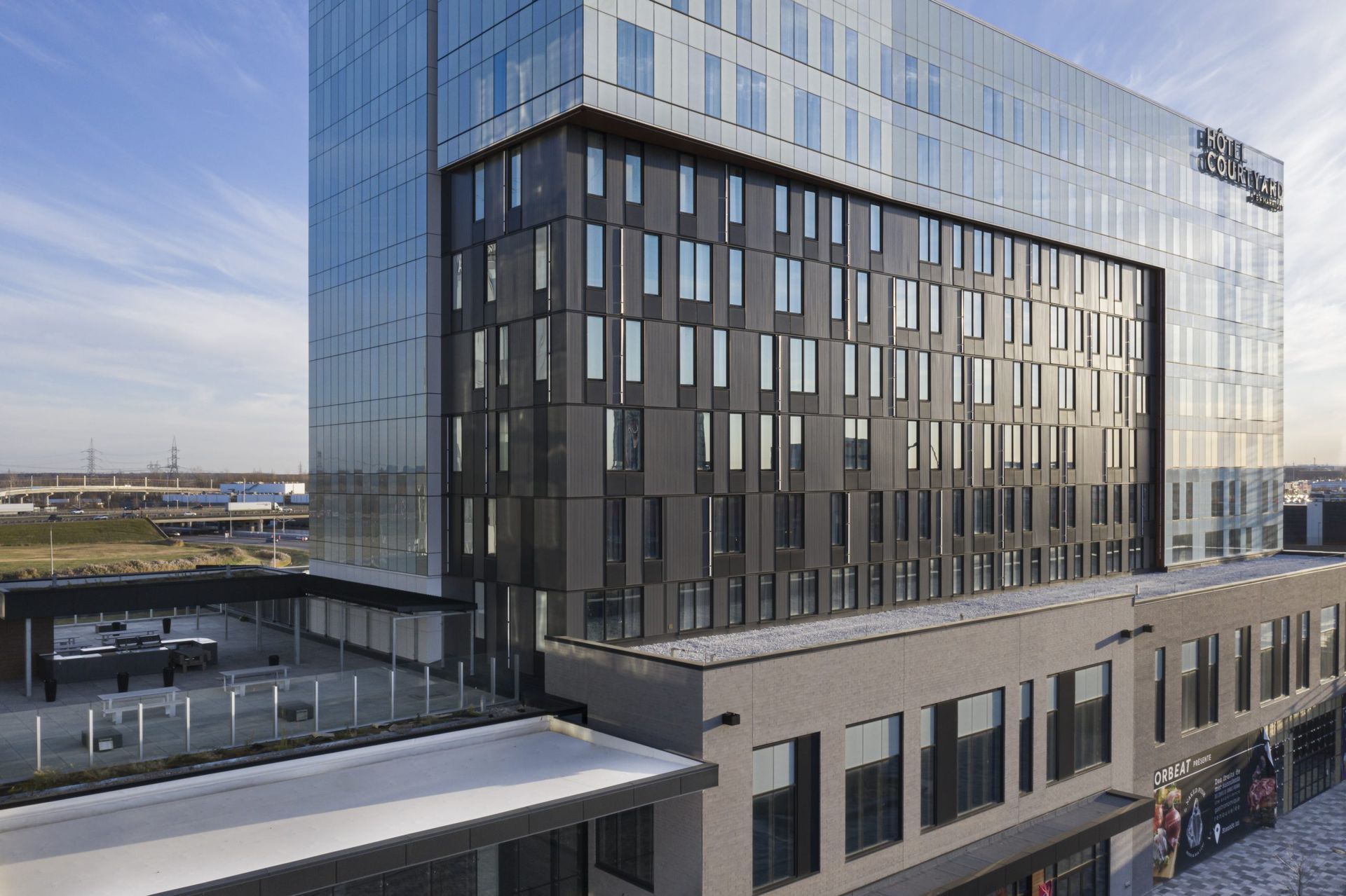 Bâtiment hôtelier moderne avec façade en verre et gris foncé, lumière du jour éclatante.