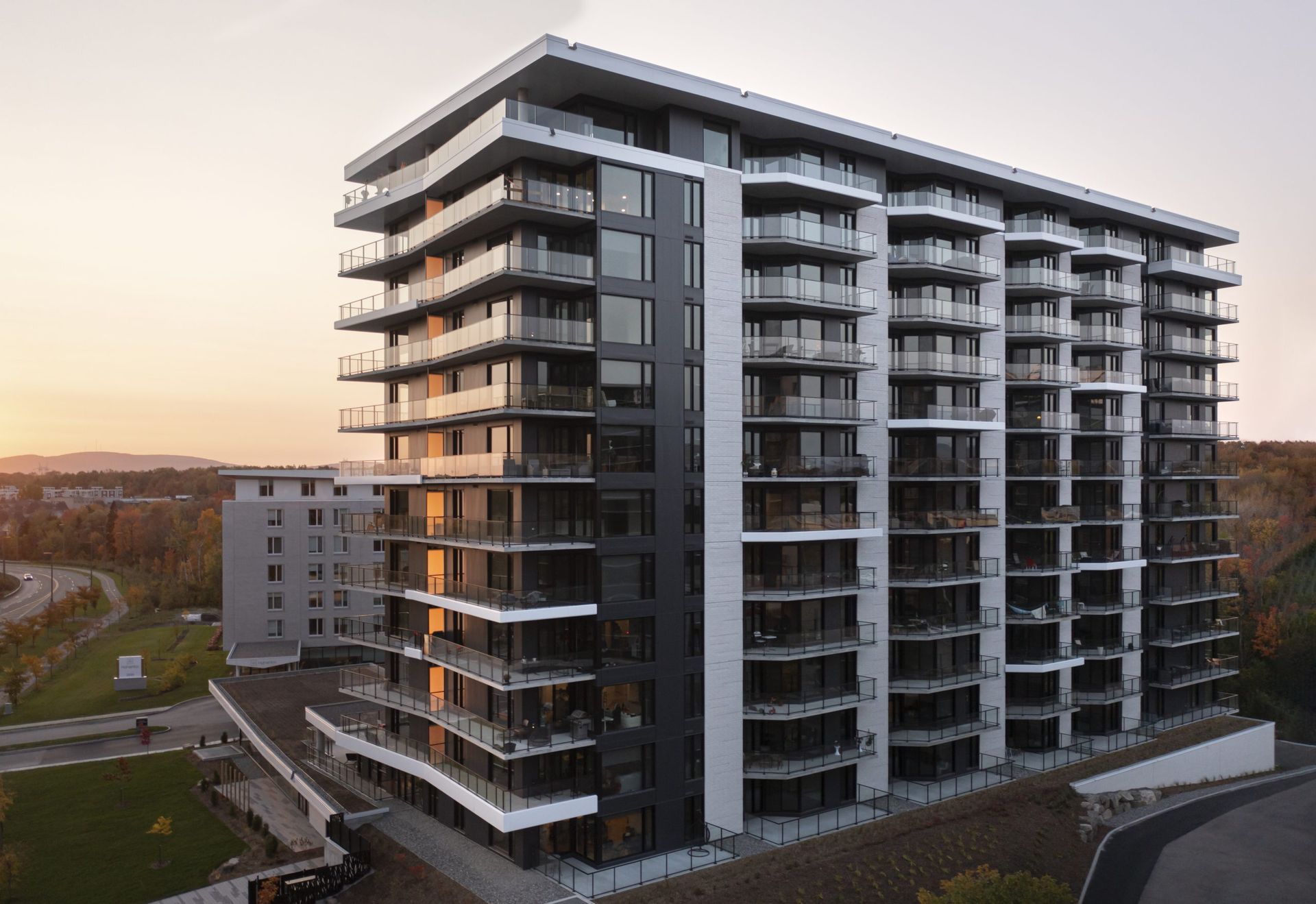 Immeuble d'appartements moderne de grande hauteur avec balcons en verre, sur fond de ciel couchant.