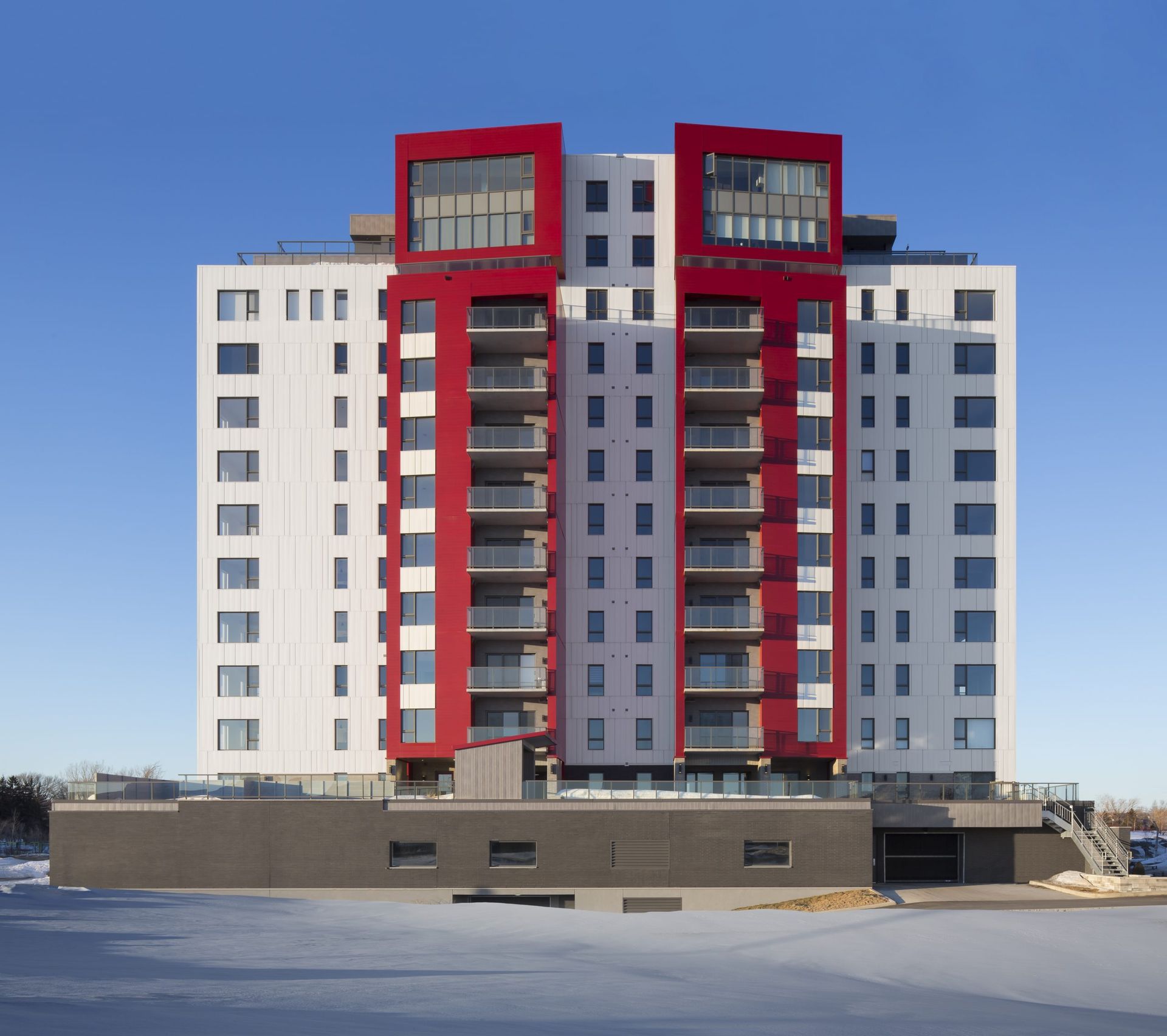 Immeuble moderne de grande hauteur avec façade blanche et rouge contre un ciel bleu clair.