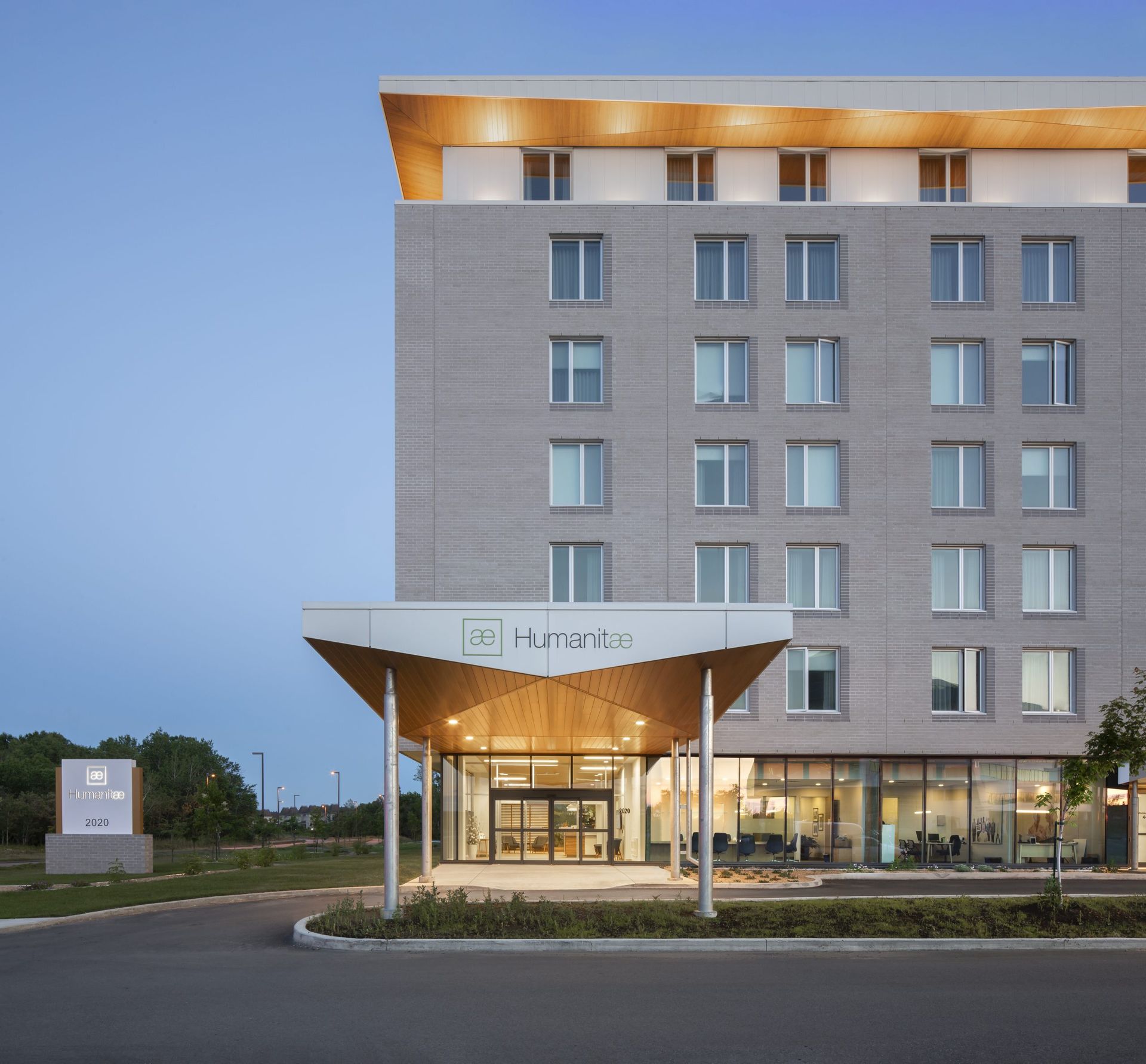 Entrée d'hôtel moderne avec un auvent, une façade grise et des portes vitrées ouvertes.