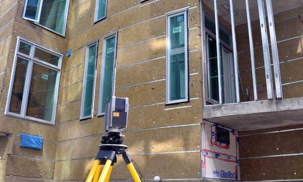 Un appareil d'arpentage sur un trépied capture des données à partir d'une façade extérieure de bâtiment avec des fenêtres.