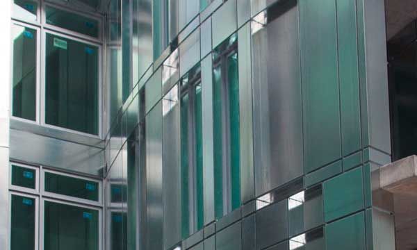 Extérieur de bâtiment brillant et moderne avec panneaux et fenêtres réfléchissants, dans des tons bleu sarcelle et gris.