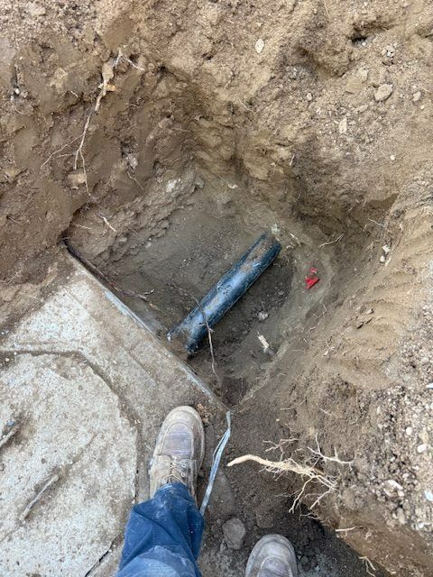 Excavation hole with exposed black pipe and a worker’s boot at the edge.