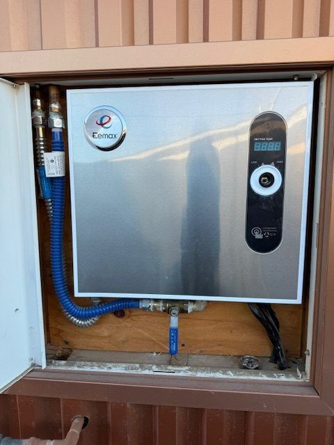 Wall-mounted water heater inside an open utility cabinet with pipes and wiring visible