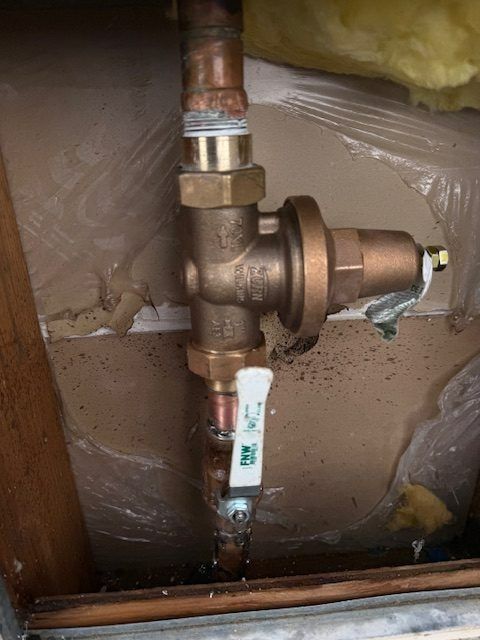 Copper plumbing valve and pipe fittings inside a wall opening, with insulation and a white shutoff handle.