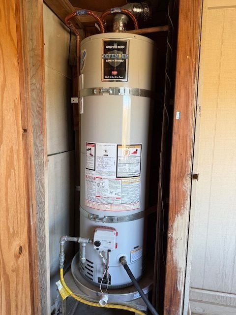 Water heater in a utility closet with pipes, valves, and labels, viewed through a doorway.