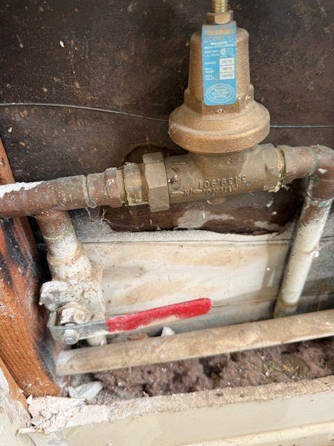 Close-up of a rusted pipe valve with a blue handle and a red shutoff lever in a wall cavity
