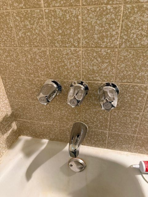 Bathroom sink with chrome faucet and three wall-mounted knobs on tan tiled wall