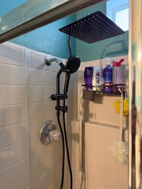 Black showerhead in a white-tiled shower with bath products on a corner shelf