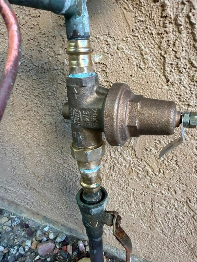 Close-up of a brass plumbing valve and pipe connection against a stucco wall.