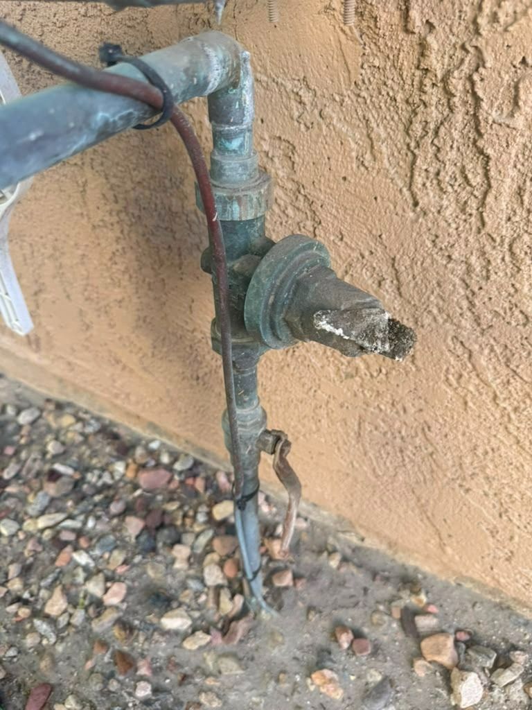 Close-up of a rusted outdoor water pipe and valve against a tan stucco wall.