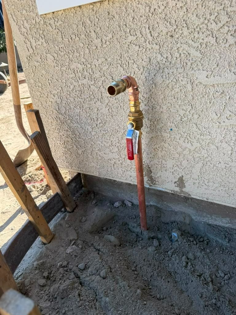 Outdoor water spigot with brass valve and red pipe against a stucco wall on a construction site