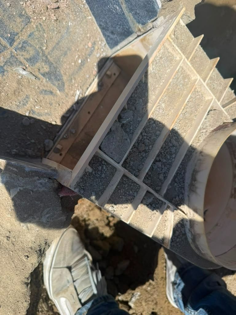 Foot stepping over a dirt-filled hole beside a concrete stair and wall outdoors