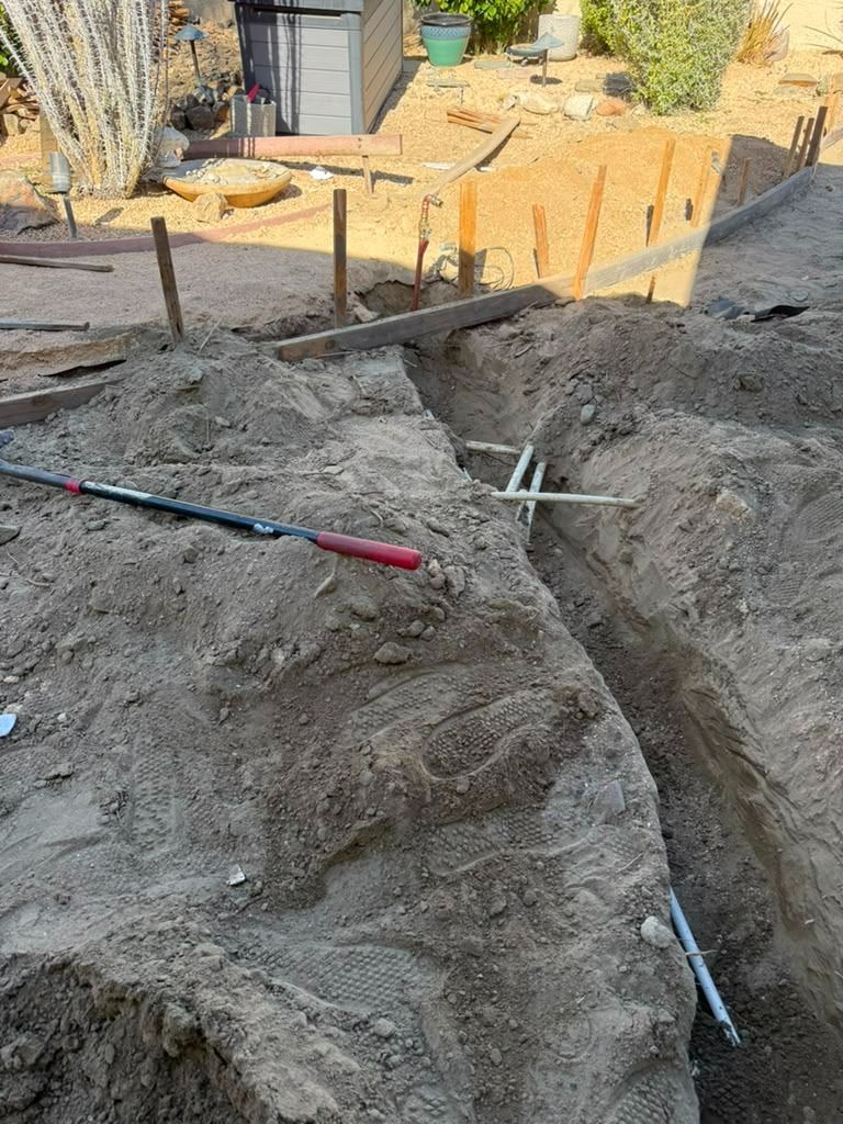 Freshly dug trench and soil at a construction site with a shovel and orange stakes