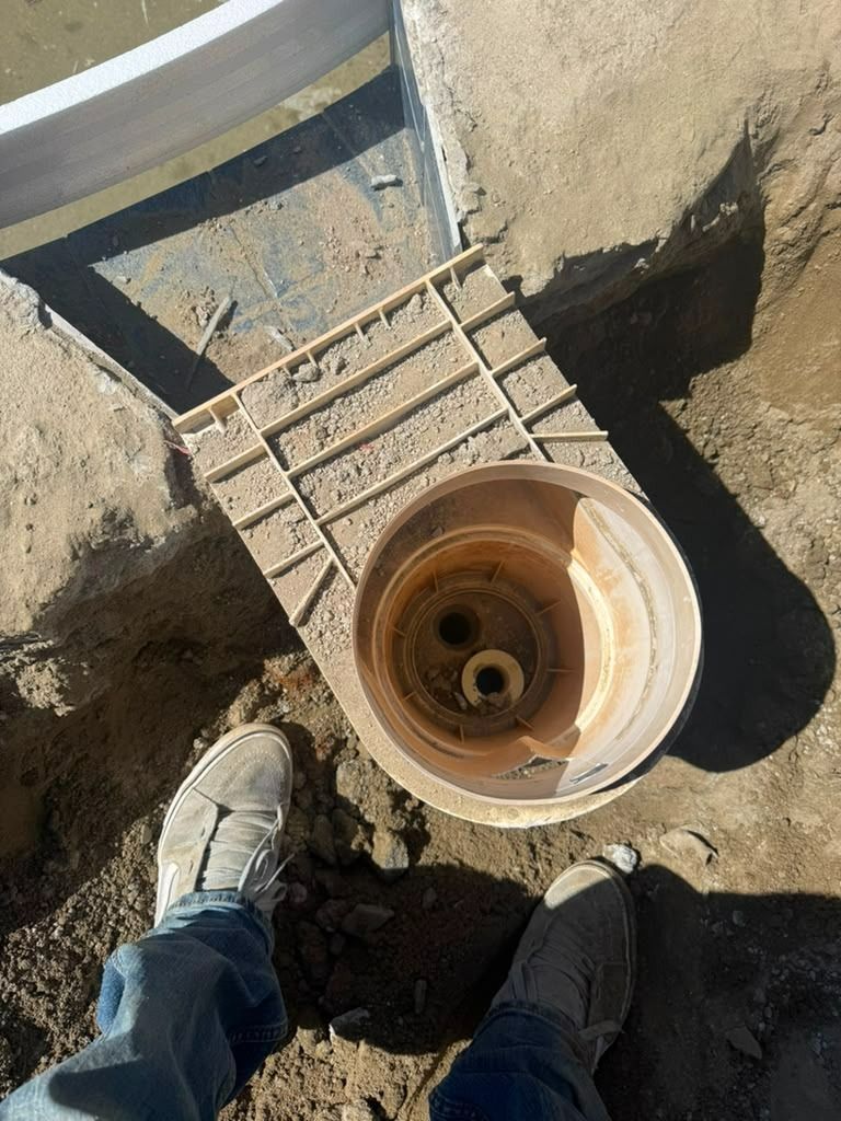 Top view of a utility hole with a ladder and two shoes at the edge of a dirt excavation