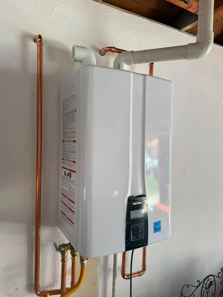 White tankless water heater mounted on a wall with copper pipes and a gray vent pipe
