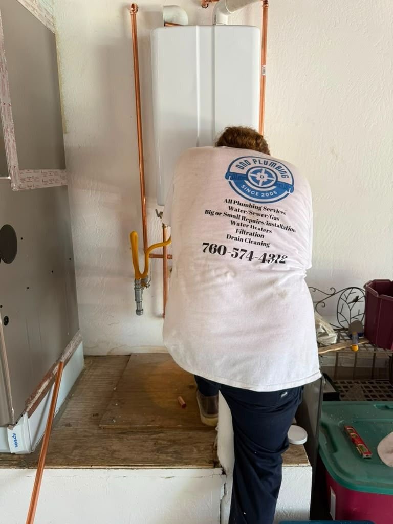 Worker in a white T-shirt installing a wall-mounted water heater in a utility room.