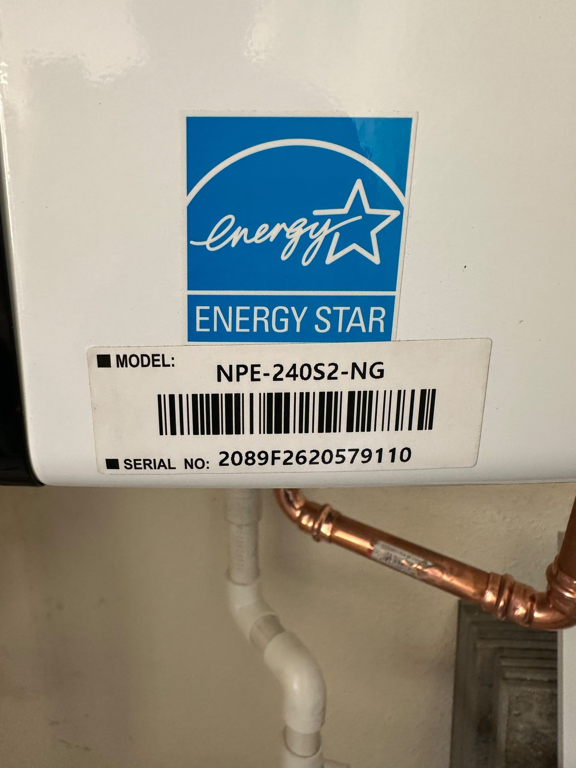 Energy Star label on white appliance with model and serial numbers above copper pipe and drain line