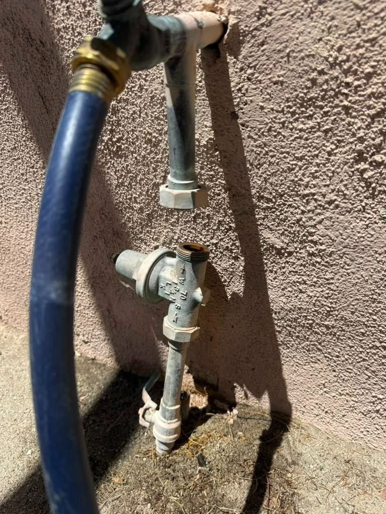 Blue hose connected to outdoor water pipes and valves against a stucco wall.
