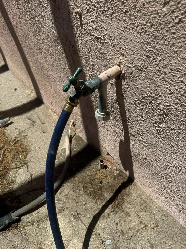 Outdoor faucet with blue hose attached to a wall spigot on a stucco exterior wall