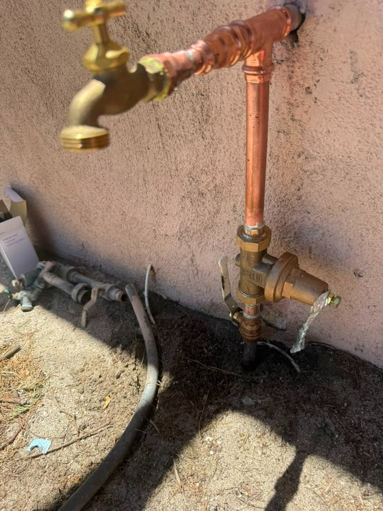 Copper outdoor plumbing pipe with faucet and valve mounted on a stucco wall