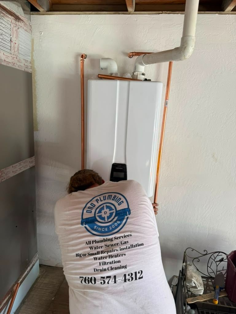 Person kneeling before a white boiler cabinet in a utility room, with exposed pipes and a bucket nearby