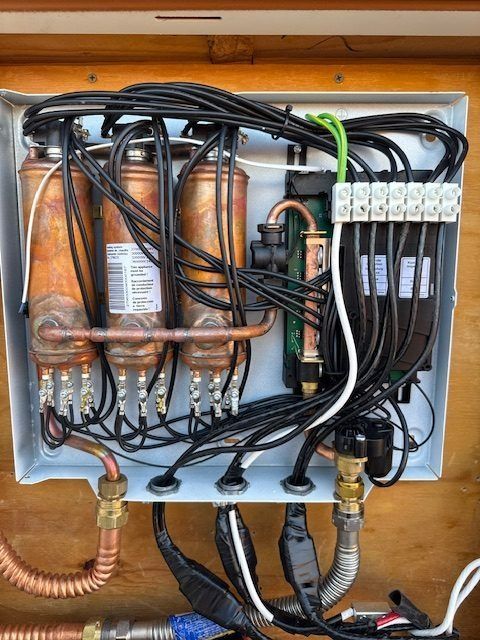Open electrical control panel with wiring, copper pipes, and connectors mounted on a wooden board