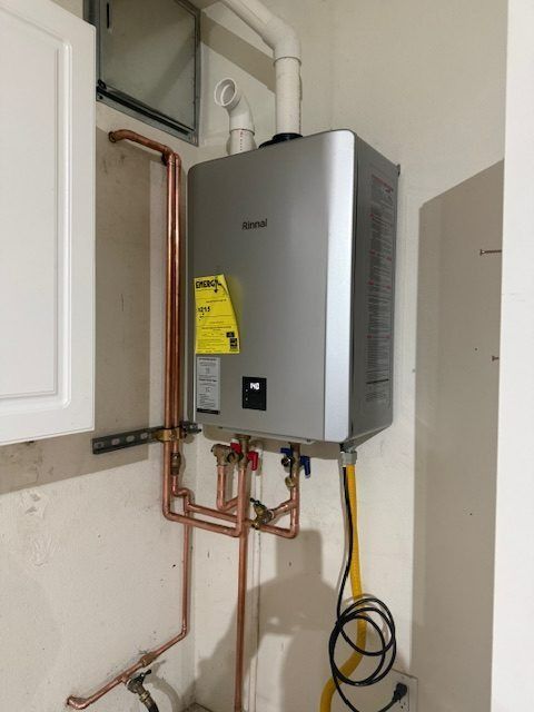 Wall-mounted gray water heater with copper pipes and yellow cord in a utility closet