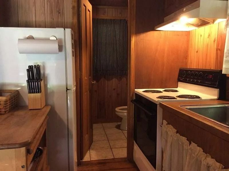 Small narrow kitchen with wood cabinets, stove, sink, and a doorway to a bathroom.