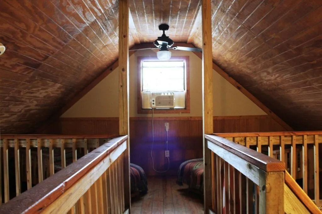 Loft hallway with wood-paneled walls, railing, ceiling fan, and a bright window at the far end