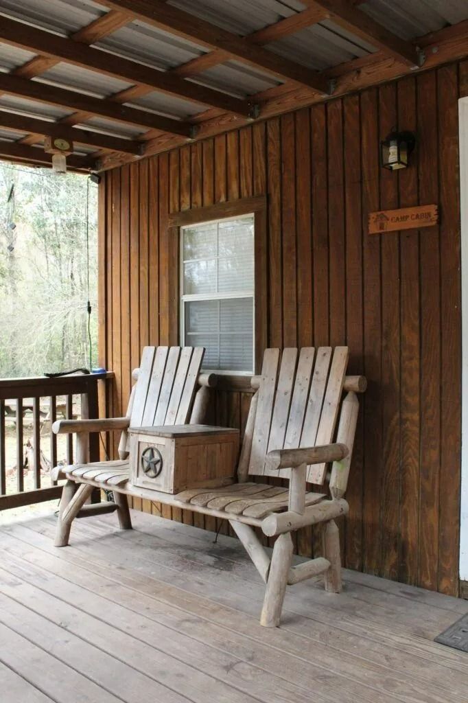 Wooden porch with rustic chairs and a small table beside a cabin wall