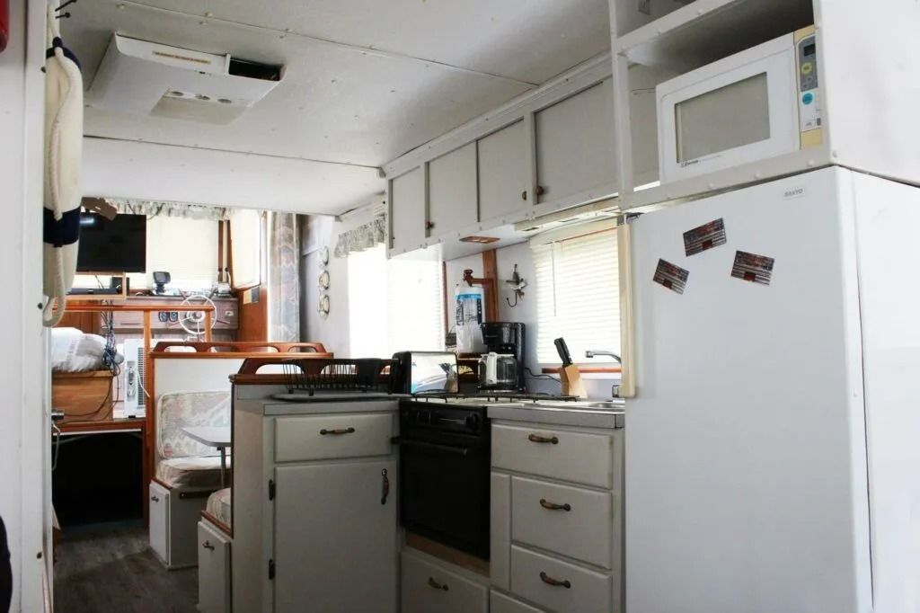 Narrow white kitchen interior with cabinets, stove, sink, and refrigerator under windows