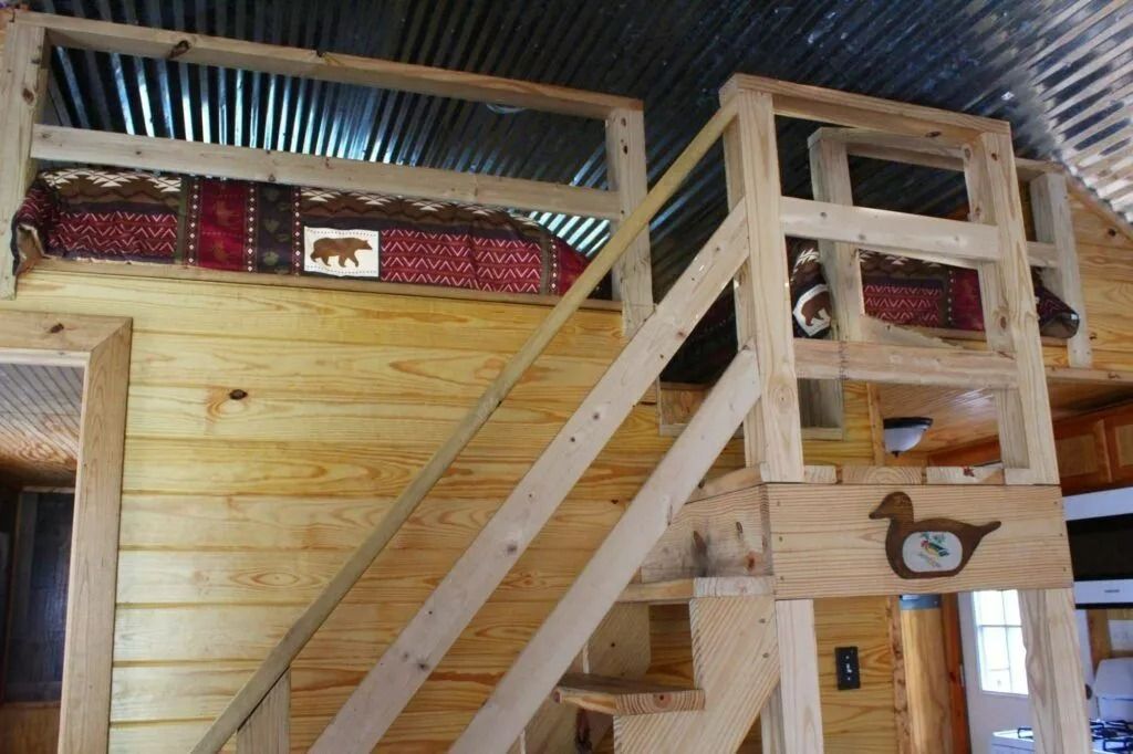 Wooden bunk loft with staircase and guardrails inside a cabin-like room