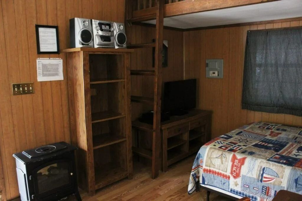 Small bedroom with wood paneling, bunk bed, desk, TV, stereo, and patterned bedspread.