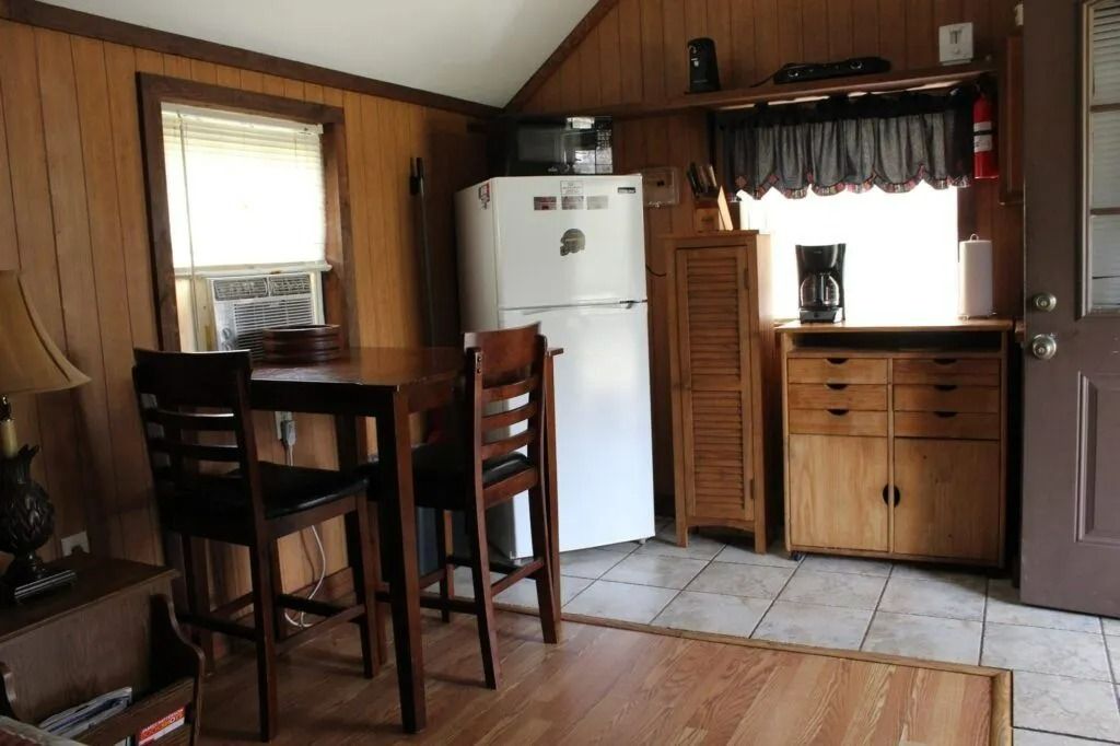 Wood-paneled kitchen with a white fridge, table and chairs, window, and wooden cabinet.