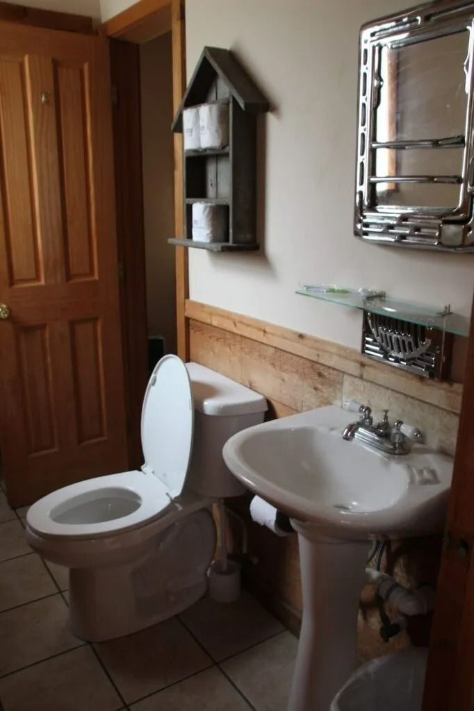Small bathroom with toilet, sink, wooden accents, wall shelf, and chrome towel rack.